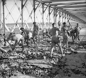 Bare backed men with picks repairing roadway over box girder bridge