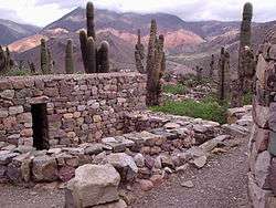 small stone structure, with cacti and mountains in the background