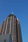 Ground-level view of a 40-story skyscraper with a tan facade and dark blue windows; a partially visible spire extends from the building's roof.