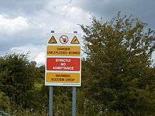 Sign warning of unexploded munitions and hazard posed by the crater.