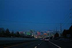 Dusk view of a freeway descending into a neon lit cityscape.