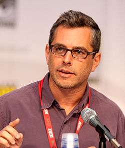 A man with glasses and black hair, talking into a microphone.