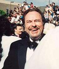 Rip Torn, a caucasian male in his early-60s with dark hair, wears a black suit and white shirt with a black bow-tie. He laughs and smiles.