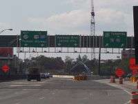 A split in a multi-lane freeway under construction with three green overhead signs. The left sign reads west Route 139 to U.S. Route 1 and 9 Interstate 280 Pulaski Skyway with two downward arrows, the middle sign reads Kennedy Boulevard Jersey City with two downward arrows, and the right sign reads New Jersey Turnpike Interstate 78 to Interstate 95 with two arrows pointing to the upper right.