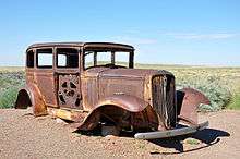 The hulk of an old car mounted on supports above a bed of gravel