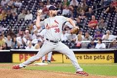 A man wearing a gray baseball uniform throwing a baseball from a dirt mound