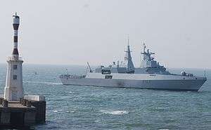 Grey ship passing a lighthouse