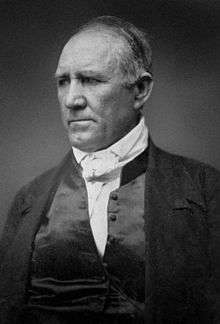 Black-and-white photograph showing a balding man from the chest up.  He is looking to the side, with a pensive expression.