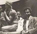 A young Sagini standing beside his statue of a nude man