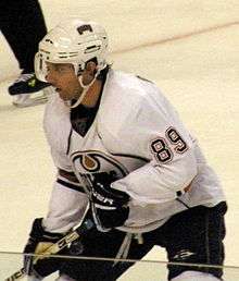 A hockey player in white Oilers uniform crouches, looking away from the camera.