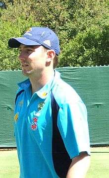 A man in a light blue and black shirt wearing a dark blue cap.