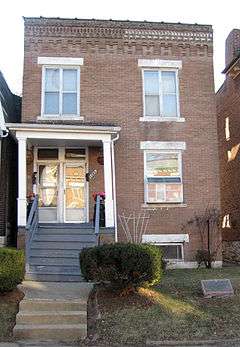 tall narrow 3 story brick building with borrom window partially below ground; steps up