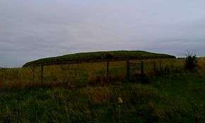 a grassy knoll, the top of which is surrounded by a stone retaining wall