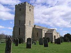 A stone church in a graveyard seen from the southwest, with a prominent battlemented tower and the body of the church and porch stretching behind it