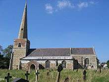 A stone church seen from the south with, from the left, a tower with a tall spire, the nave with a protruding aisle and a porch, and a shorter chancel