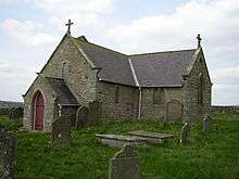 A small stone church seen from the southwest with a south transept as large as the nave