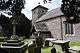 A square base of three stone steps supporting a stone block and simple cross, surrounded by gravestones and tombs