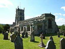 A stone church seen from the southeast, with embattled parapets on the aisle, nave and chancel and on the west tower.