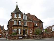 A red bricked building with a spired roof, windows and a black door