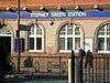 A red-bricked building with a rectangular, dark blue sign reading "STEPNEY GREEN STATION" in white letters and a man walking in front