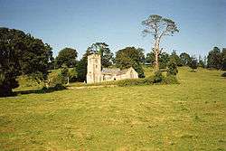 Yellow stone building with square tower set in green fields.