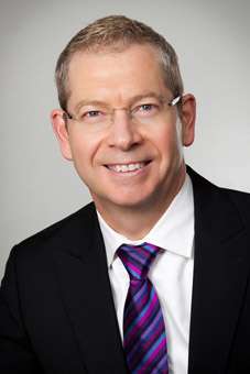 A man smiles while wearing a black suit