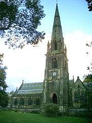 A Gothic style church dominated by a large, elaborate tower with a spire and pinnacles.