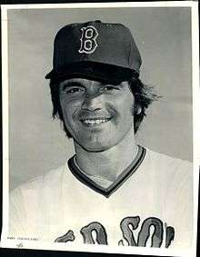 A black-and-white photo of a man's head and chest. He is wearing a baseball cap with the letter "B" and a white baseball jersey that says "RED SOX", partially obscured.