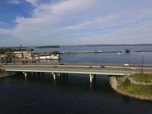 The bridge is in the foreground, with Casco Bay behind it. The Back Bay Footpath is underneath the bridge on the right, and some islands are in the background.