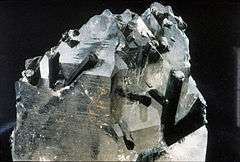 Dark bluish and green or black, rod-like tourmaline crystals emerging from clear quartz holding matrix.