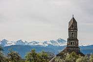 The tower of a church and snowy mountains in the distance