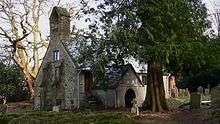 A simple chapel behind a large tree, with a bellcote and a protruding porch