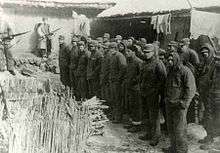 A group of men under guard standing in front of a camera