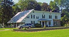 A long white house with some stone at the back and a pointed, sloping roof at the front