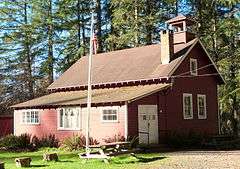 Photograph of the Venersborg School, a small, red, one-and-one-half story gabled building with a cupola and bell, in a forested setting