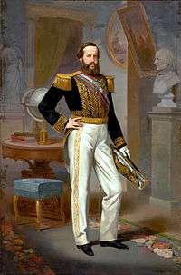 Full-length painted portrait of a young, full-bearded man standing before a table on which are books and a globe and wearing white trousers, a military tunic with heavy gold braid, a sash of office, and holding a bicorn admiral's hat