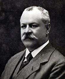 A middle-aged, mustached caucasian man, wearing a business suit