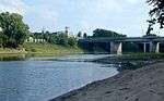 A middle-sized river with sandy and grassy banks flows under a bridge