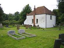 A white-painted simple chapel with a brick chimney stack and a red tiled roof. On the front are two sash windows, and a similar window is on the side at a higher level.