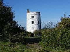 White circular building with three windows, surrounded by vegetation.