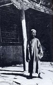 A black-and-white picture of an elderly Chinese man in front of a building