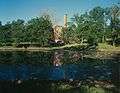 building with high chimney hidden behind trees, water in foreground