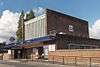 A red-bricked building with a rectangular, dark blue sign reading "WEST ACTON STATION" in white letters all under a blue sky with white clouds