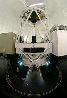 White metal truss frame inside white dome atop a circular base and flanked by two rectangular boxes on either side.