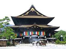 A large wooden building with an added pent roof enclosure and a Chinese style gable.